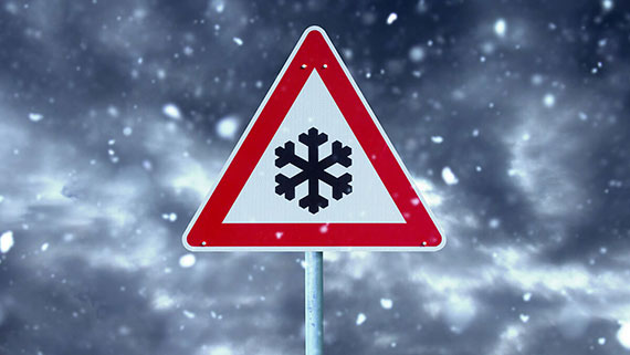 An icy roads caution sign on side of snowy road