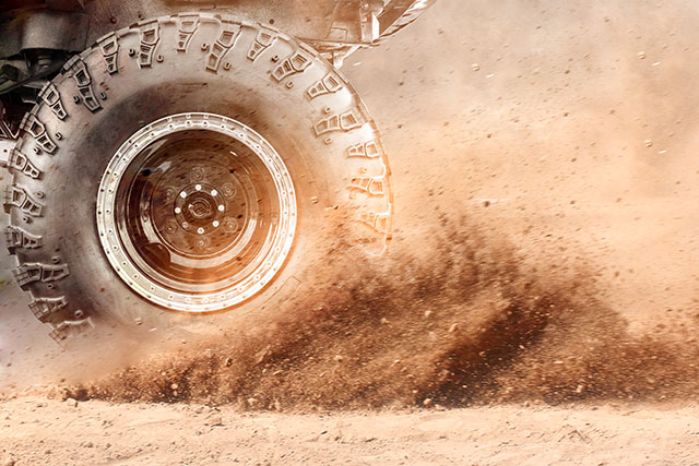 An off-road vehicle tire kicks up dirt.