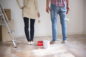 Couple looking at white wall with paint supplies around them