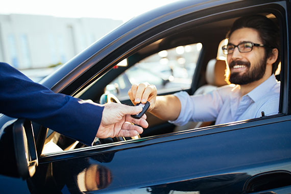 A man being handed a keyfob while sitting in a shiny new car